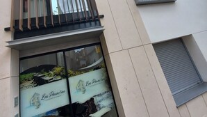 Eine moderne Gebäudefassade mit großen Fenstern, einem Metallbalkon und einer kleinen Klimaanlage.