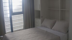 Ein Schlafzimmer mit einem Bett, einem Kleiderschrank und einem Fenster mit Vorhängen.