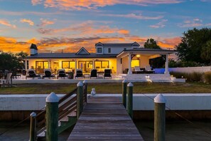 A waterfront property with a covered patio, outdoor seating, and a wooden dock leading to the house.