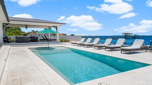 Une piscine dotée de chaises longues et d’un espace de repos couvert, avec vue sur une étendue d’eau.