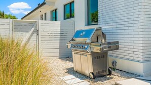 Un barbecue est installé devant une maison blanche en briques, dont l’entrée est fermée par un portail.