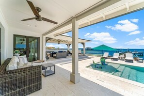 A covered outdoor area with a pool, lounge chairs, and a view of the ocean.
