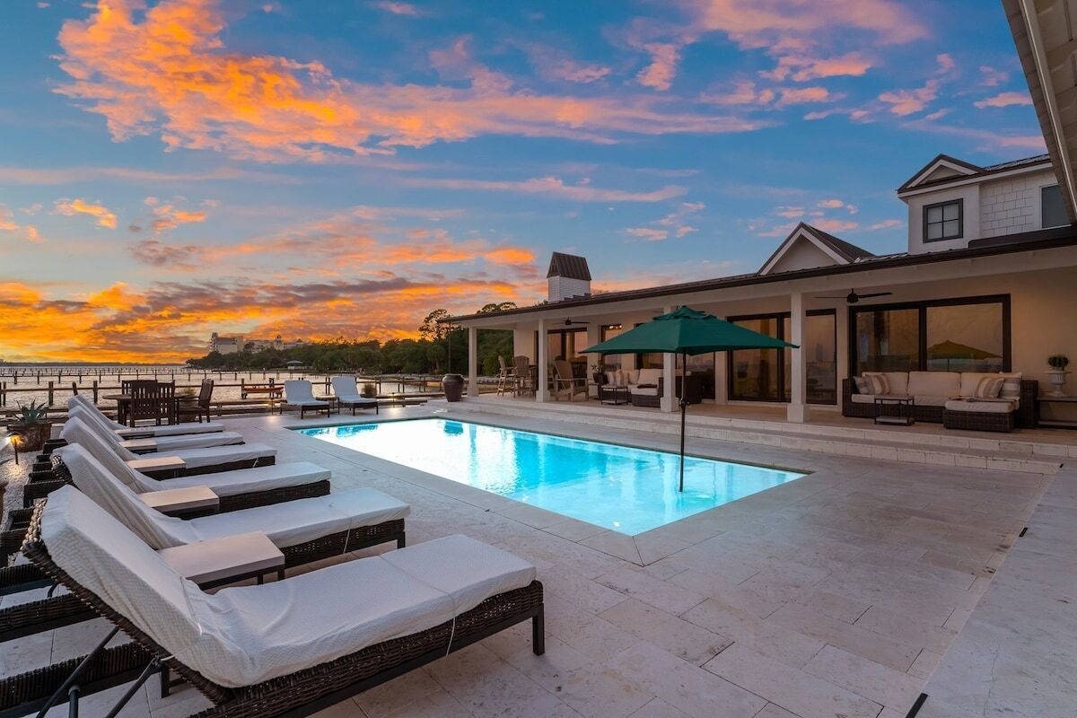 A swimming pool with lounge chairs, a covered seating area, and a view of the sunset.