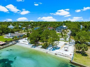 An aerial view of a coastal property with a beach, houses, and a pier.