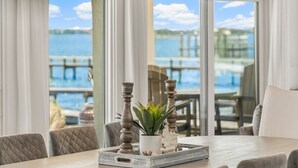 A dining area with a table set for two, featuring a tray with a potted plant and candle holders, overlooking a body of water and dock. - Waterfront Sunsets~ Private Dock ~ Heated pool! (Panama City)