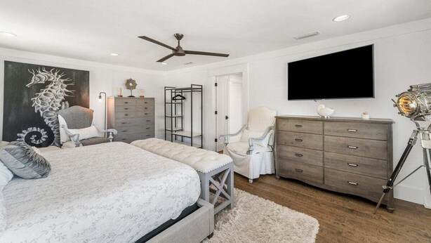 Une chambre à coucher comprenant un lit, un bureau, une chaise, une commode, un téléviseur et un ventilateur de plafond.