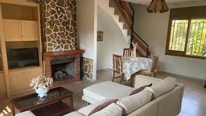 Ein Wohnzimmer mit Kamin, einer Couch, einem Esstisch mit Stühlen und einer Treppe.