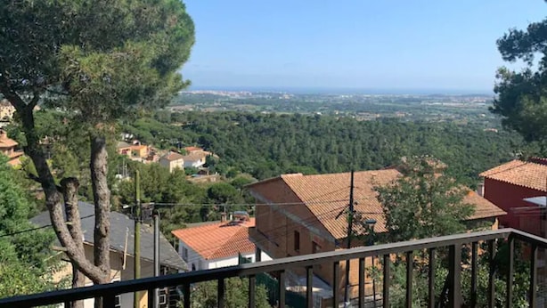 Blick von einem Balkon auf ein Dorf mit terrakottafarbenen Dächern und üppiger Vegetation.