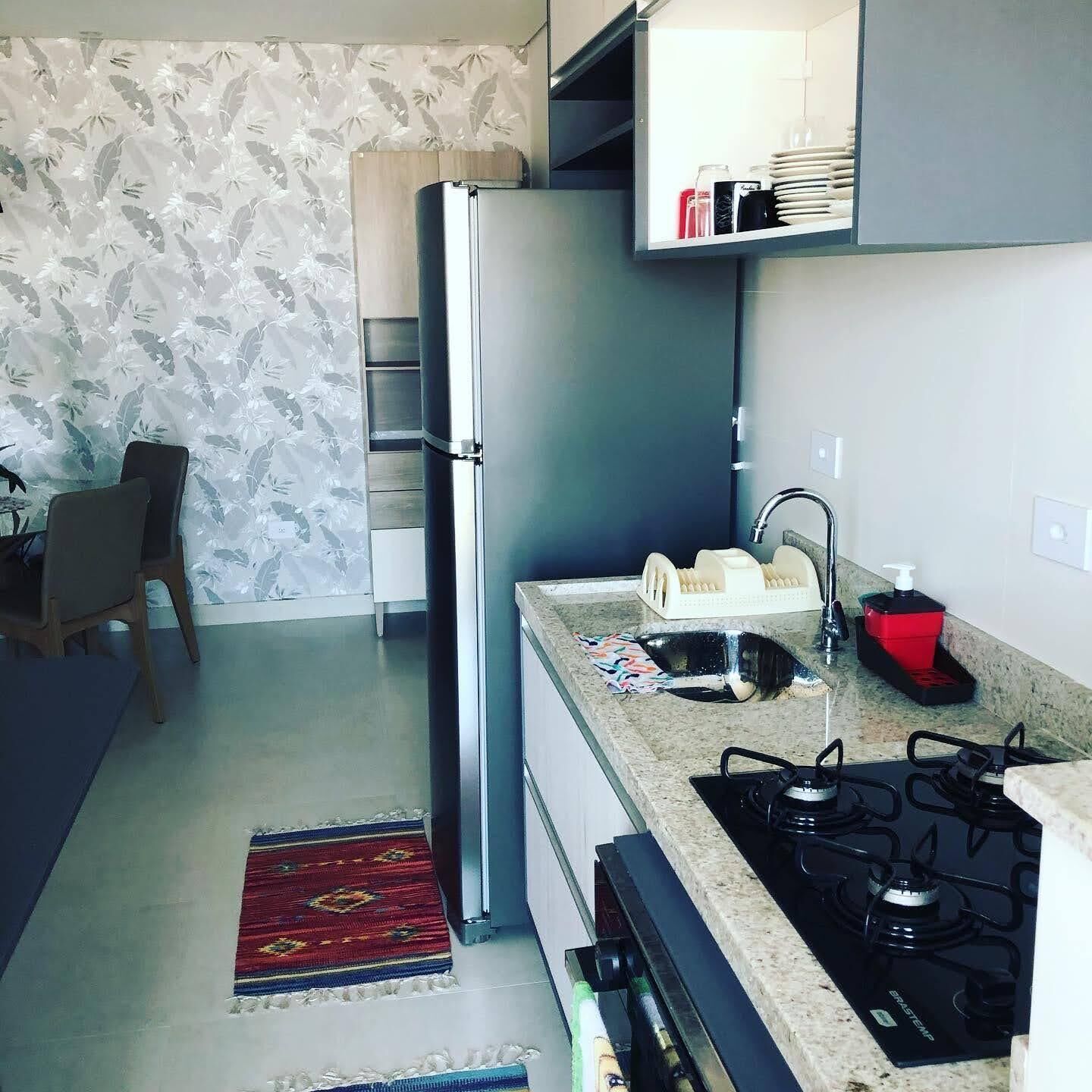 Cocina compacta con refrigerador, pileta, estufa y un pequeño comedor con una silla y mesa.