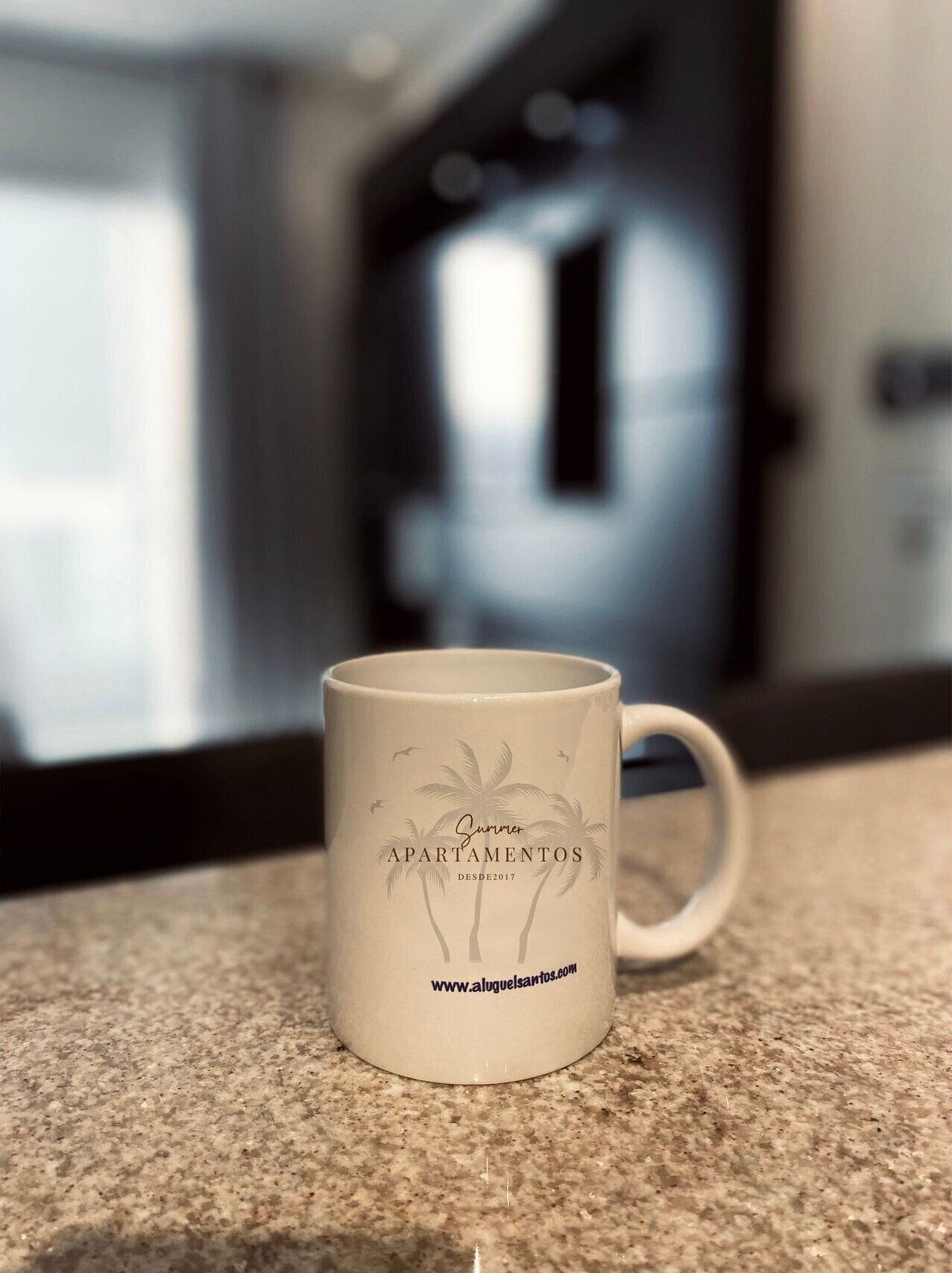 Una taza color beige con diseño de palmera y texto sobre una encimera de cocina.