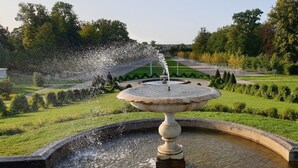 Une fontaine avec des jets d’eau, située dans un jardin à la française.