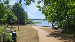 Un chemin pavé mène à une zone au bord du lac, aménagée avec des bancs et des tables de pique-nique.
