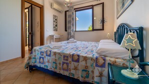 Un dormitorio con cama, mesita de noche, ventana y puerta.