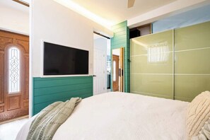Une chambre à coucher avec un lit, un téléviseur fixé au mur et une armoire verte.