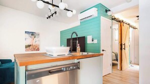 A compact kitchen with a dishwasher, a teal accent wall, a wooden countertop, and a ceiling light fixture. - Tiny House Apt in Little Italy w OffStreet Parking (Wilmington)