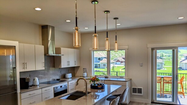 Une cuisine moderne dotée d’un îlot central, d’appareils électroménagers en acier inoxydable et de luminaires suspendus.
