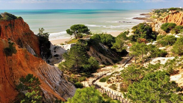 Un paisaje costero con playa, acantilados y un camino que lleva a un edificio.