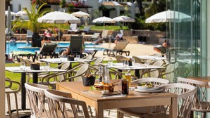 Un área de comedor junto a la piscina con mesas, sillas y sombrillas.