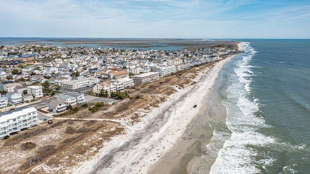 An aerial view of a coastal residential area with houses along the beach, a clear sky, and a calm sea.