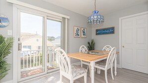 A dining area with a wooden table and white chairs, a blue chandelier, and a sliding glass door leading to a balcony.