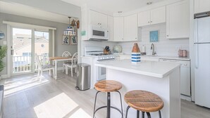 A modern kitchen with white cabinetry, a central island with stools, a stainless steel sink, and a microwave.