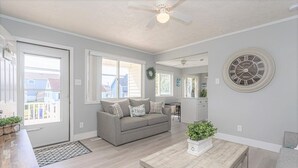 A spacious living room with a grey sofa, a wooden coffee table, and a large wall clock.