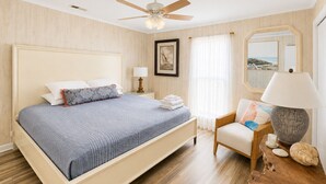 A bedroom with a bed, a chair, a nightstand, a lamp, and a ceiling fan. - *Beach House!!*Views!!*Steps to Ocean!*Amenities! (Oak Island)
