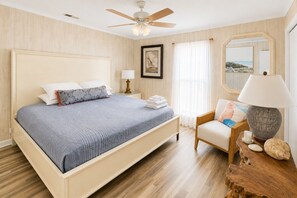 A bedroom with a bed, a chair, a nightstand, a lamp, and a ceiling fan.