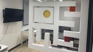 A modern living room with a flat-screen TV mounted on the wall, a white entertainment unit with a circular decorative piece, and a grey sofa with a red accent piece.
