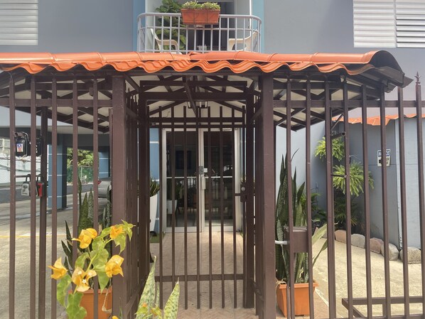 A gated entrance with a metal gate, potted plants, and a building entrance with a tiled roof.