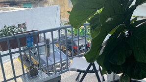 A balcony with a potted plant, a chair, and a view of parked cars and buildings.