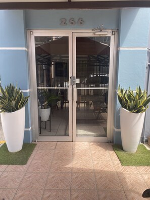 A building entrance with a glass door, number 266, potted plants, and a tiled floor.