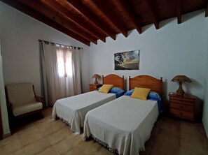 Une chambre avec deux lits simples, une chaise, une table de chevet avec une lampe et un tableau au mur.