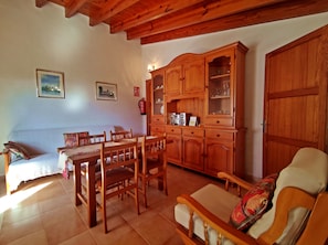 Uma sala de estar aconchegante com uma mesa de jantar de madeira, cadeiras, um sofá e um armário com portas de vidro.