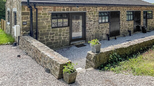 Un bâtiment en pierre avec un toit en tuiles, une entrée en pierre et un petit jardin agrémenté de gravier et de plantes.