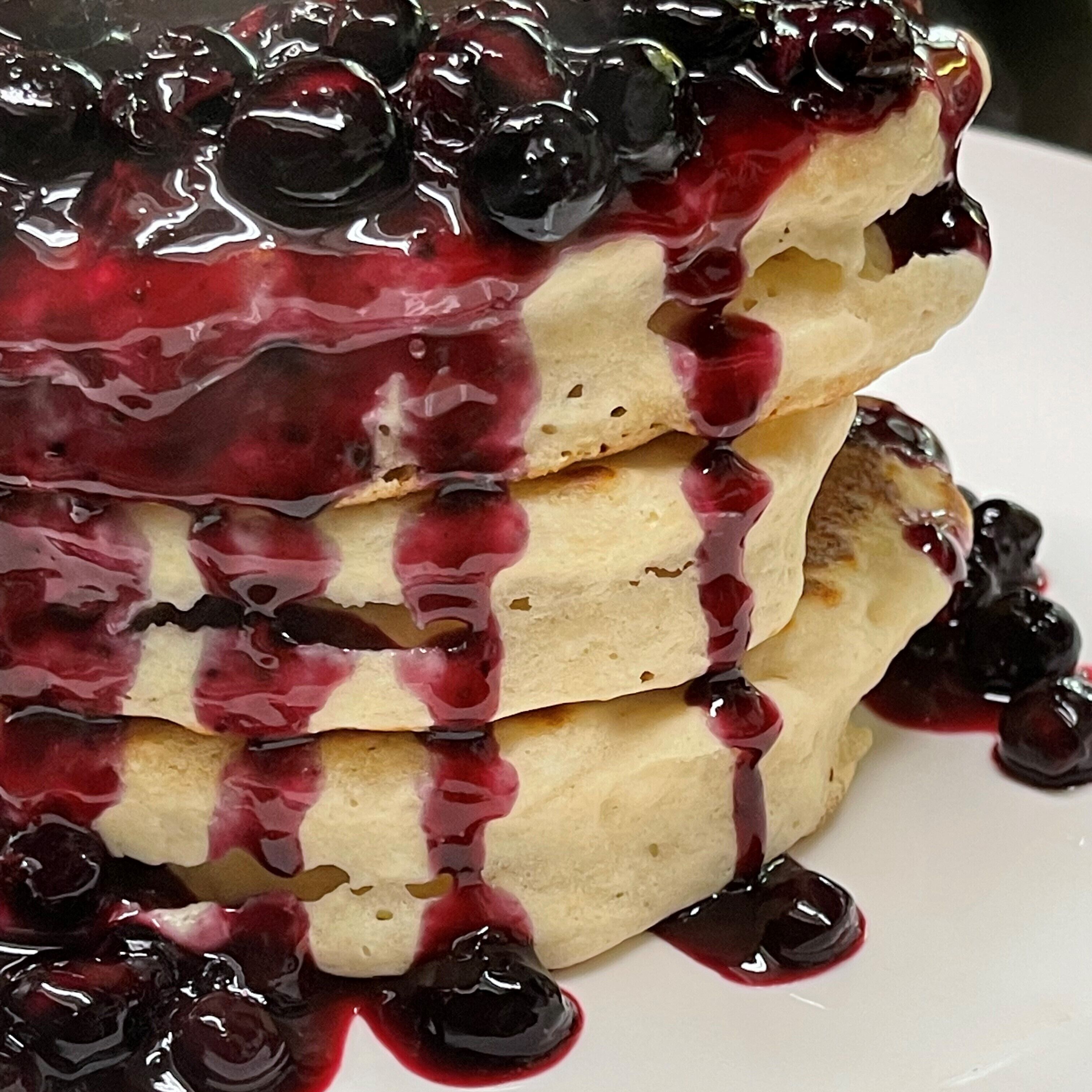 A stack of pancakes with blueberry sauce and berries on a white plate.