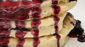 A stack of pancakes with blueberry sauce and berries on a white plate.