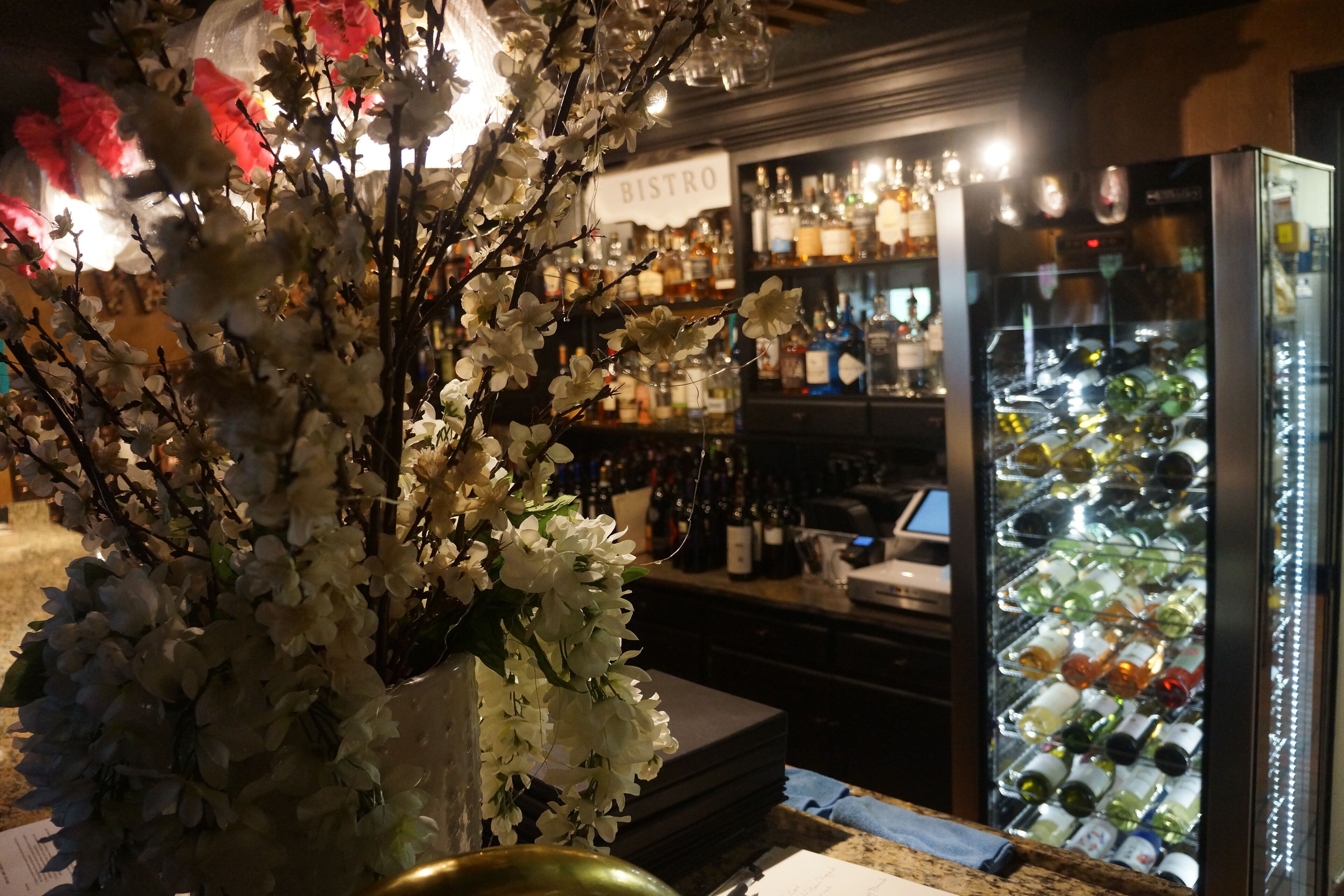 Una zona de bar con un cartel que dice 'BISTRO', varias botellas y un mostrador refrigerado.