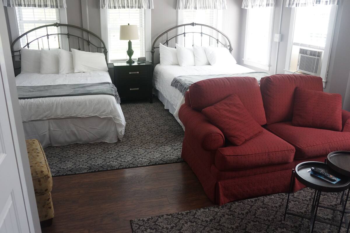 Ein Schlafzimmer mit zwei Betten, einem roten Sessel, einem kleinen Tisch mit Fernbedienung und einem gemusterten Teppich.