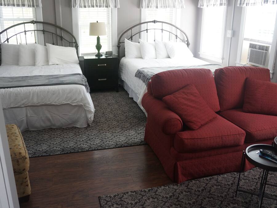 Un dormitorio con dos camas, un sillón rojo, una mesita con un control remoto y una alfombra estampada.