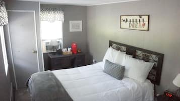 Quarto de hotel com cama, mesa de cabeceira, abajur, relógio de parede e quadro emoldurado.