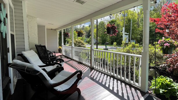 A covered porch with two black and white lounge chairs, a white railing, and hanging flower baskets. - The Frogtown Inn (Canadensis)