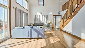 Un salon spacieux avec un grand canapé, un escalier en bois et une vue sur l’extérieur grâce à de grandes fenêtres.