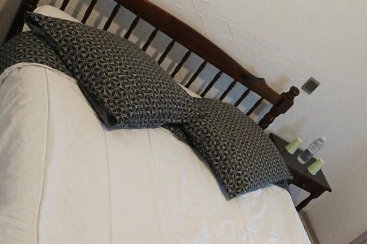 Een bed met een houten hoofdbord, wit beddengoed en een gestreept kussen.
