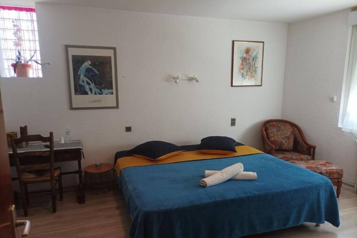 Een slaapkamer met een bed, een stoel, een bureau en twee kunstwerken in een lijst aan de muur.