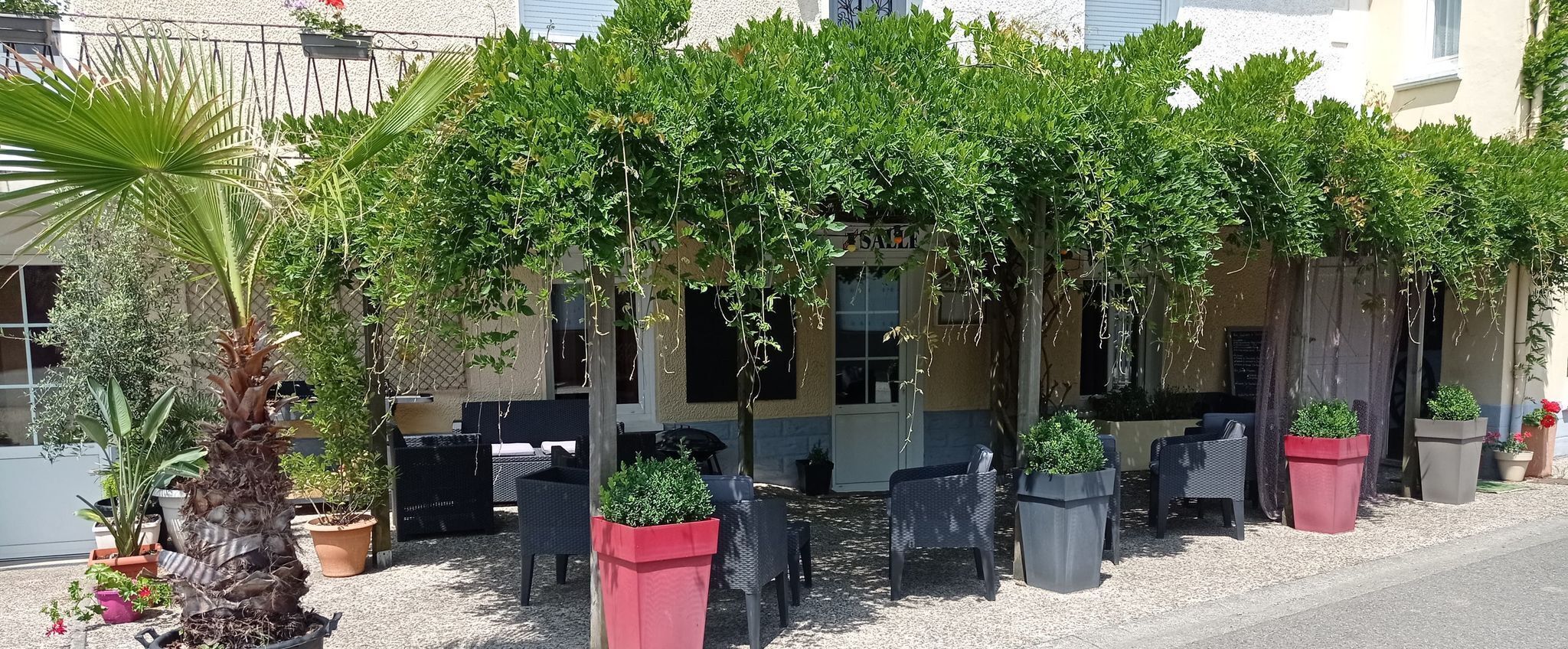 An outdoor seating area with wicker furniture and potted plants, a palm tree, and a building with a 'SALE' sign.