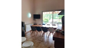 A dining area with a round table and chairs, a television on the wall, and a view of the outdoors. - Maison Familiale, South Aveyron 5minutes from St Rome de Tarn beach  (Saint-Rome-de-Tarn)