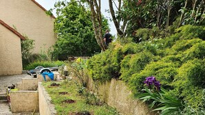 A garden with a stone pathway, various plants, and a blue tarp on a vehicle. - Maison Familiale, South Aveyron 5minutes from St Rome de Tarn beach  (Saint-Rome-de-Tarn)