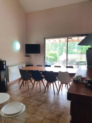 Un coin repas avec une table ronde et des chaises, un téléviseur fixé au mur et une vue sur l’extérieur.