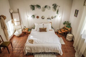 Une chambre avec un grand lit, une échelle en bois, une petite table avec des livres et une plante en pot.